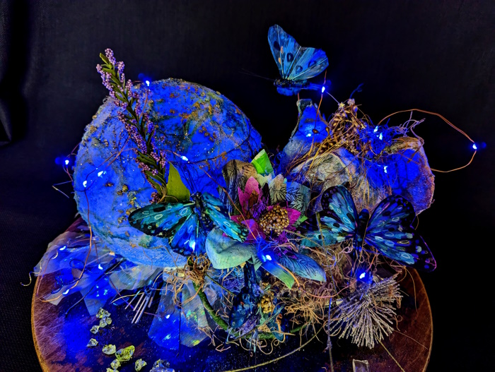 This is a photo of a 3D sculpture with angels and a glowing blue orb placed on a rotating base.This is one of a series of works that attempt to capture creation from the beginning.