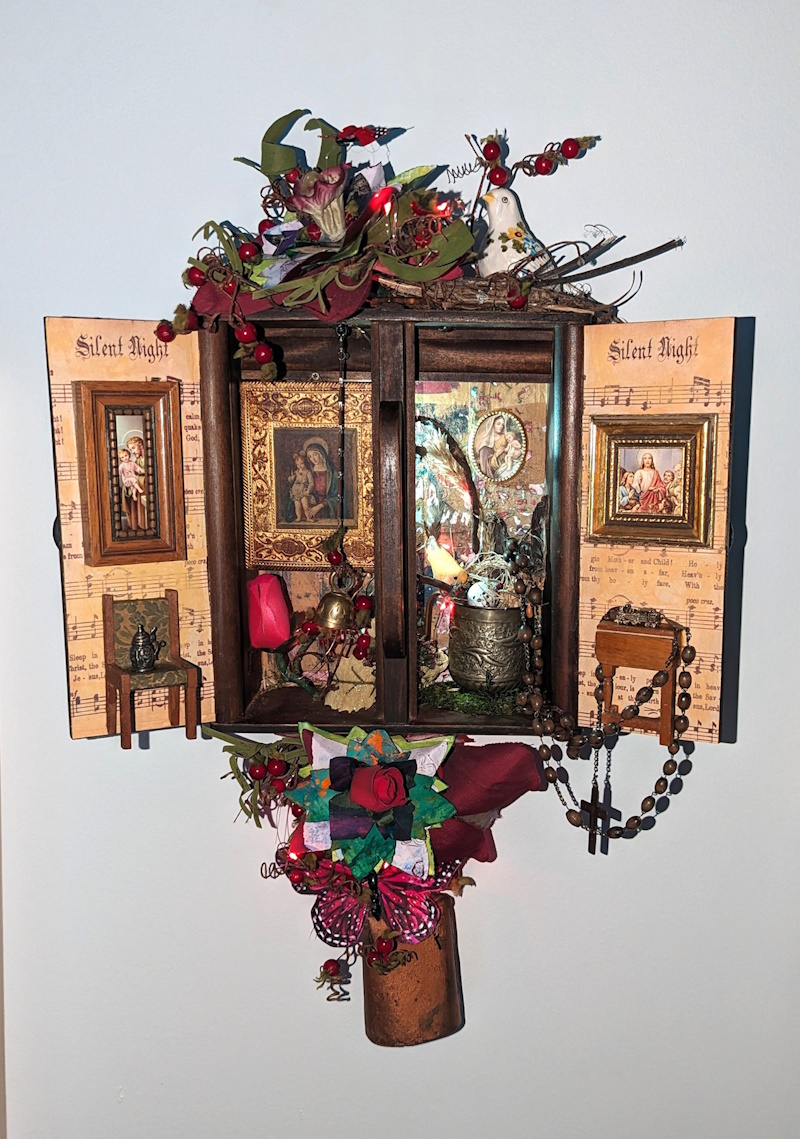 This is a 3D wall hanging sculpture of a miniature world built inside a tiny wall cabinet. It has a variety of religious items inside it as well as dollhouse miniatures. It is lit by LED lights for capturing miniature worlds and creating a sense of liminal magic.